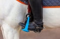 The foot of the rider, sitting on a white horse, in a black boot with a spur, rests on a safe plastic stirrup. Close-up Royalty Free Stock Photo