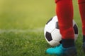 Football ball and footballer in red socks and cleats standing on a grass pitch Royalty Free Stock Photo