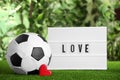 Football ball, lightbox with word Love and heart on green grass against blurred background Royalty Free Stock Photo