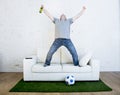 Football fan watching tv match on sofa with grass pitch carpet celebrating goal Royalty Free Stock Photo