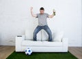 Football fan watching tv match on sofa with grass pitch carpet celebrating goal Royalty Free Stock Photo