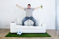 Football fan watching tv match on sofa with grass pitch carpet celebrating goal Royalty Free Stock Photo