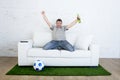 Football fan watching tv match on sofa with grass pitch carpet celebrating goal Royalty Free Stock Photo