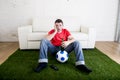 Football fan watching tv sitting off couch on grass carpet with ball emulating stadium pitch Royalty Free Stock Photo
