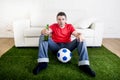 Football fan watching tv sitting off couch on grass carpet with Royalty Free Stock Photo
