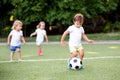 Team of toddlers playing soccer on green field, three friends in the middle of game, smiling kid is dribbling ball at front Royalty Free Stock Photo