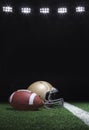 Football and helmet on grass field below stadium lights at night Royalty Free Stock Photo