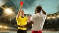 Football referee showing a player a red card for breaking rules at crowded stadium over night cloudy sky. Royalty Free Stock Photo