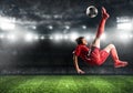 Soccer striker in red uniform hits the ball with an acrobatic kick in the air at the stadium Royalty Free Stock Photo