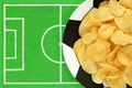 Football soccer party table with snacks. Salted potato chips on plate like soccer ball, on small football field background