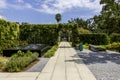 a footpath in the garden with a black marble water fountain and lush green trees and plants and colorful flowers, blue sky Royalty Free Stock Photo