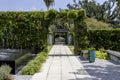 a footpath in the garden with a black marble water fountain and lush green trees and plants and colorful flowers, blue sky