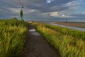 Footpath through the salt marshes at the German North Sea coast in Fedderwardersiel under scenic cloudy sky