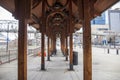 A footpath underneath a brown wooden pergola at a bus station with black metal benches and trash cans on a cloudy day in Nashville