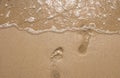 Footprints at the beach in sand from walking barefoot going to transparent water with foam.
