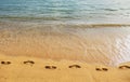 Footprints at golden sand, footsteps. Blue ocean wave on sandy beach. Beach in sunset summer time. Beach landscape