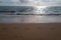 Footprints at golden sand, footsteps. Blue ocean wave on sandy beach. Beach in sunset summer time. Beach landscape