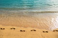 Footprints at golden sand, footsteps. Blue ocean wave on sandy beach. Beach in sunset summer time. Beach landscape