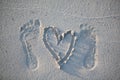 Footprints of the groom and the bride`s feet and a painted heart on the sand of the beach. Royalty Free Stock Photo