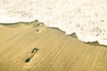 Footprints of naked barefoot at beach against upcoming wave foam