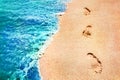 Footprints of the people on a golden pink sand on the sea coast. Soft waves of blue and green color. Marine creative background cl Royalty Free Stock Photo