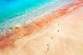 Footprints of the people on a golden pink sand on the sea coast. Soft waves of pink, red and blue color. Multicolores sea water. Royalty Free Stock Photo