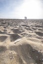 Footprints on sand beach along sea at day, two people walk in the distance a silhouette against a blue sky. Scheveningen Royalty Free Stock Photo