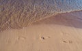 Footprints in the sand with small wave approaching