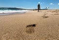 Footprints in the sand with walking woman in distance Royalty Free Stock Photo