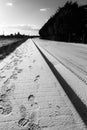 Footprints on a sidewalk covered by snow near a long road Royalty Free Stock Photo