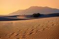 Footprints of three travelers are swept away by the wind in the desert. Mountains and blue sea in the distance