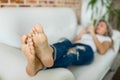 Foots of young woman in jeans using smart phone lying on white sofa