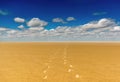 Footsteps in desert sand with blue sky and clouds