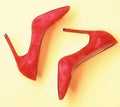 Footwear with thin high heels, stiletto shoes, top view. Shoes made out of red suede on yellow background. Pair of