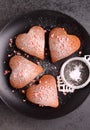 Fore cupcakes in heart with powdered sugar on a black plate.