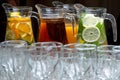 In the foreground is a blurry image of glasses, in the background are jugs with different lemonades