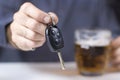 In the foreground car keys kept in a male hand. A beer mug in the background