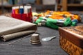 In the foreground a needle lying on a thimble. In the background, fabric and multicolored mouline threads and sewing threads.