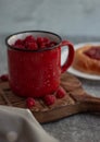 In the foreground is a red mug with garden raspberries, in the background a cheesecake with berry filling, light background, defoc