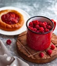 In the foreground is a red mug with garden raspberries, in the background a cheesecake with berry filling, light background, defoc