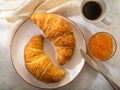 In the foreground there are two croissants, a cup of coffee, orange jam in a glass vase. The knife is on the edge of the plate. Royalty Free Stock Photo