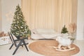 In the foreground is a toy swing sheep. Christmas interior in the living room with beige sofa and Christmas trees with