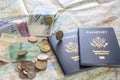 foreign coins falling onto paper currency and two American passports laying on large open map