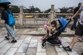 A foreign girl sitting in a stroller holding a toy and passing by on the Wende Bridge