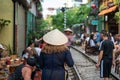 Foreign tourist with Vietnamese conical hat walking on railroad in Hanoi. People drink coffee or walking on railways waiting for