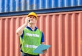 Foreman in hard hat and safety vest talks on two-way radio at containers cargo