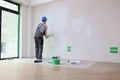 Foreman paints wall in white with roller dipped in bucket