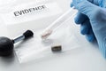 Forensic scientist`s hand holding glass tube over evidence bag next to brush