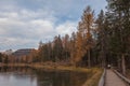 Forest with autumnal colors around a Dolomite lake crossed by a wooden walkway