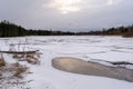 The forest lake is covered with snow-covered broken ice. Layers of cracked ice on a body of water. Early spring in a coniferous